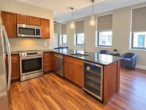 A modern kitchen with wooden cabinets, stainless steel appliances, a large island, and pendant lighting. - Downtown Suite - Spacious! RnRHoF, Casino, Stadium (Cleveland)