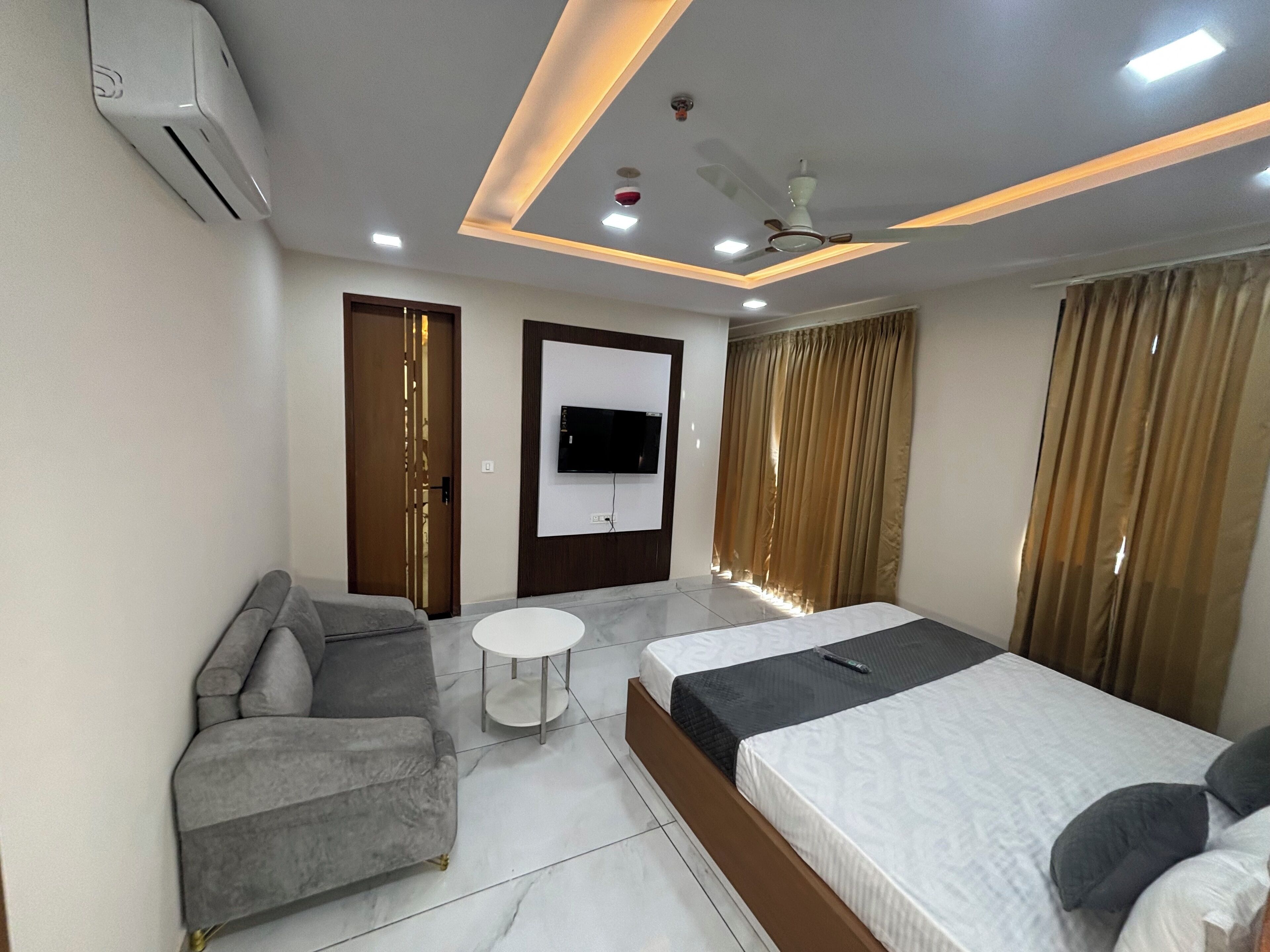 Une chambre d’hôtel moderne équipée d’un canapé, d’un lit, d’une petite table, d’une télévision et d’un ventilateur de plafond.