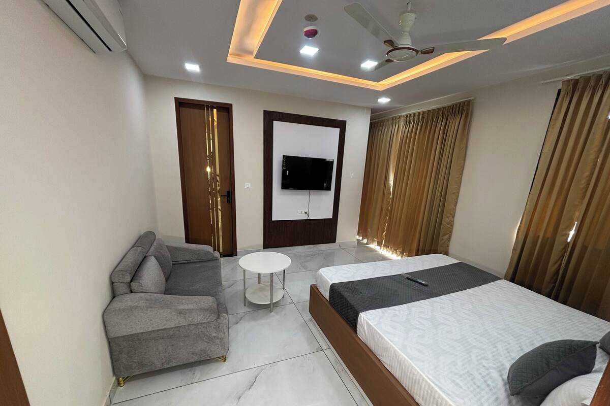 A modern hotel room with a sofa, a bed, a small table, and a TV mounted on the wall.