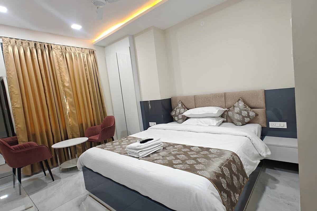 A modern hotel room with a bed, a small table, a chair, and a curtain.