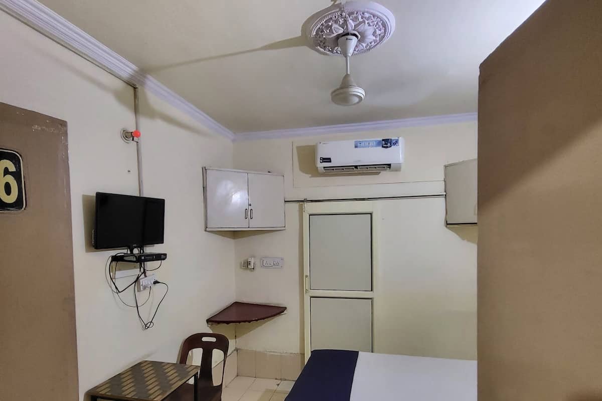 Una habitación de hotel con cama, escritorio, silla, televisor, equipo de aire acondicionado y ventilador de techo.