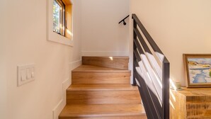 Una scala in legno con ringhiera nera, una finestra a sinistra e un quadro a destra.