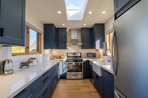 A modern kitchen with dark cabinets, stainless steel appliances, and a skylight. - Modern 2BR Heart of South Park Walkable With W/D (San Diego)