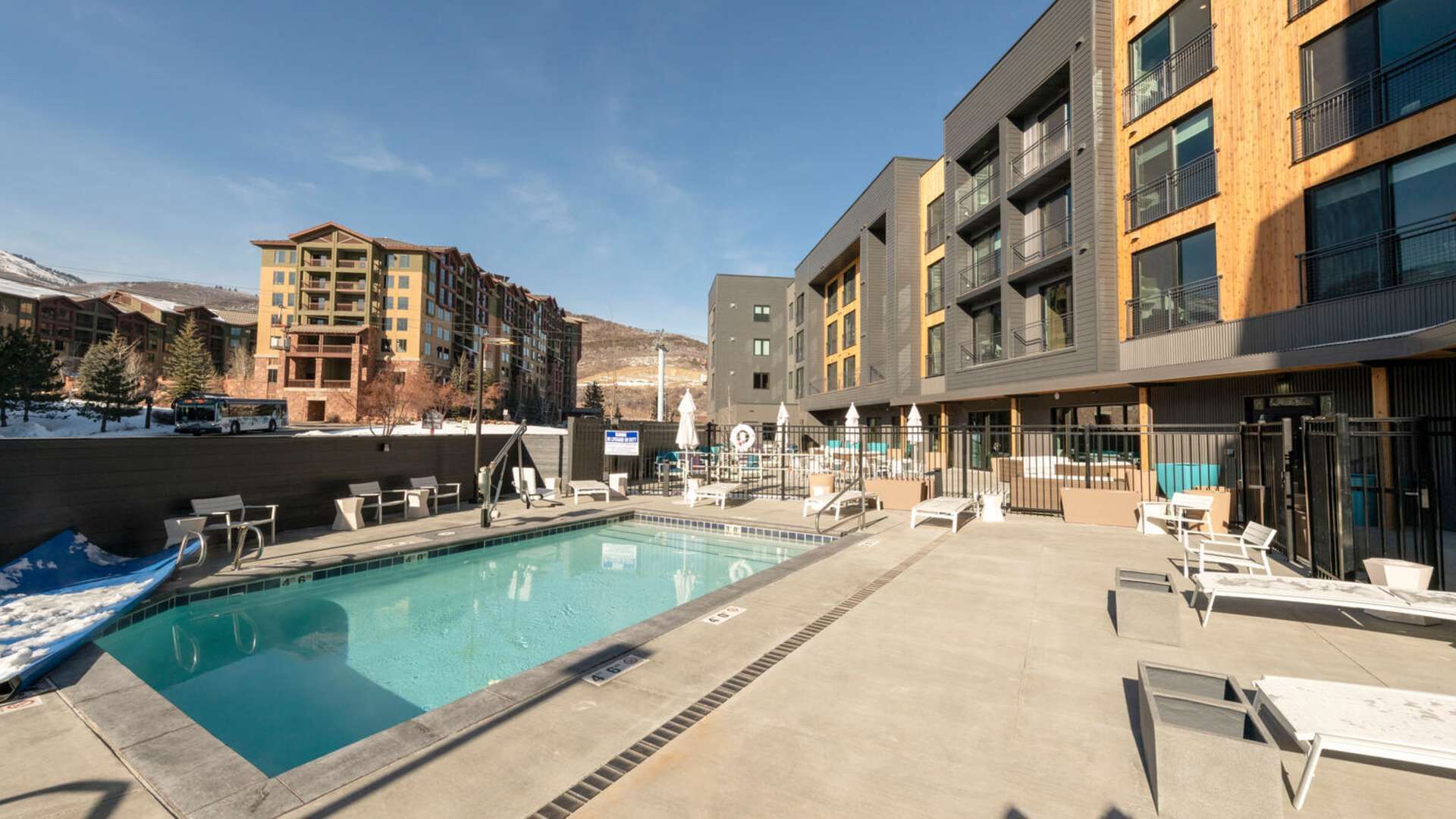 A pool area with a diving board, lounge chairs, and a view of surrounding buildings.