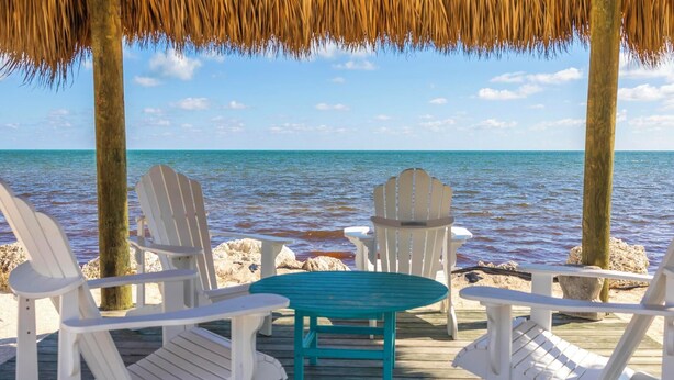 A wooden deck with white Adirondack chairs and a turquoise table, overlooking a calm sea. - Suntastic -  Salt Water Lagoon Front 2 Bedroom in popular OCEAN FRONT Kawama (Key Largo)