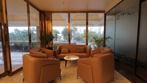 Un espace de détente moderne avec des canapés et des fauteuils en cuir, une table basse ronde et de grandes fenêtres offrant une vue sur la ville.