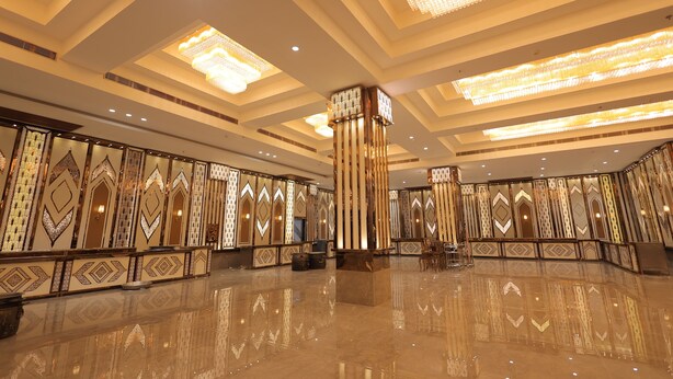 Un hall d’entrée spacieux doté d’un sol réfléchissant, de panneaux muraux décoratifs et de plusieurs lustres.