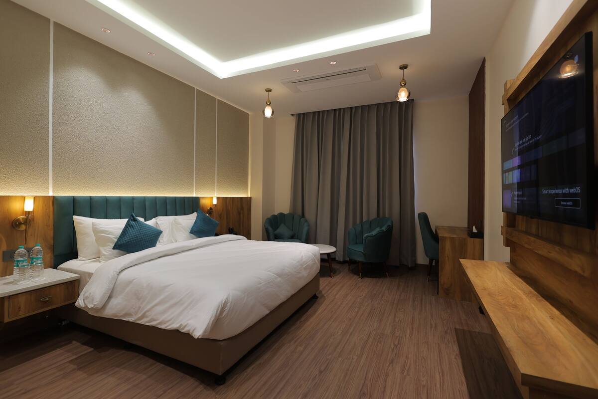 A modern hotel room with a large bed, two armchairs, a wooden desk, and a flat-screen TV.