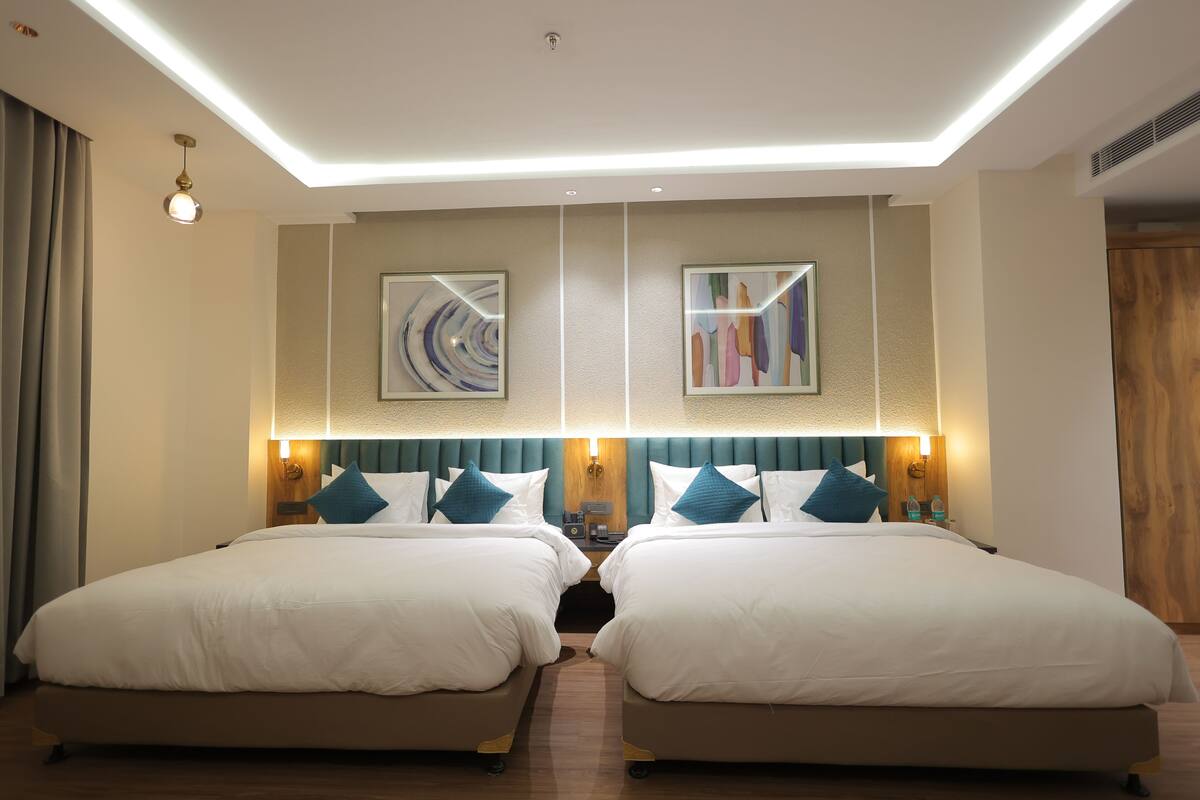 A hotel room with two beds, a ceiling light, and two wall-mounted lamps.