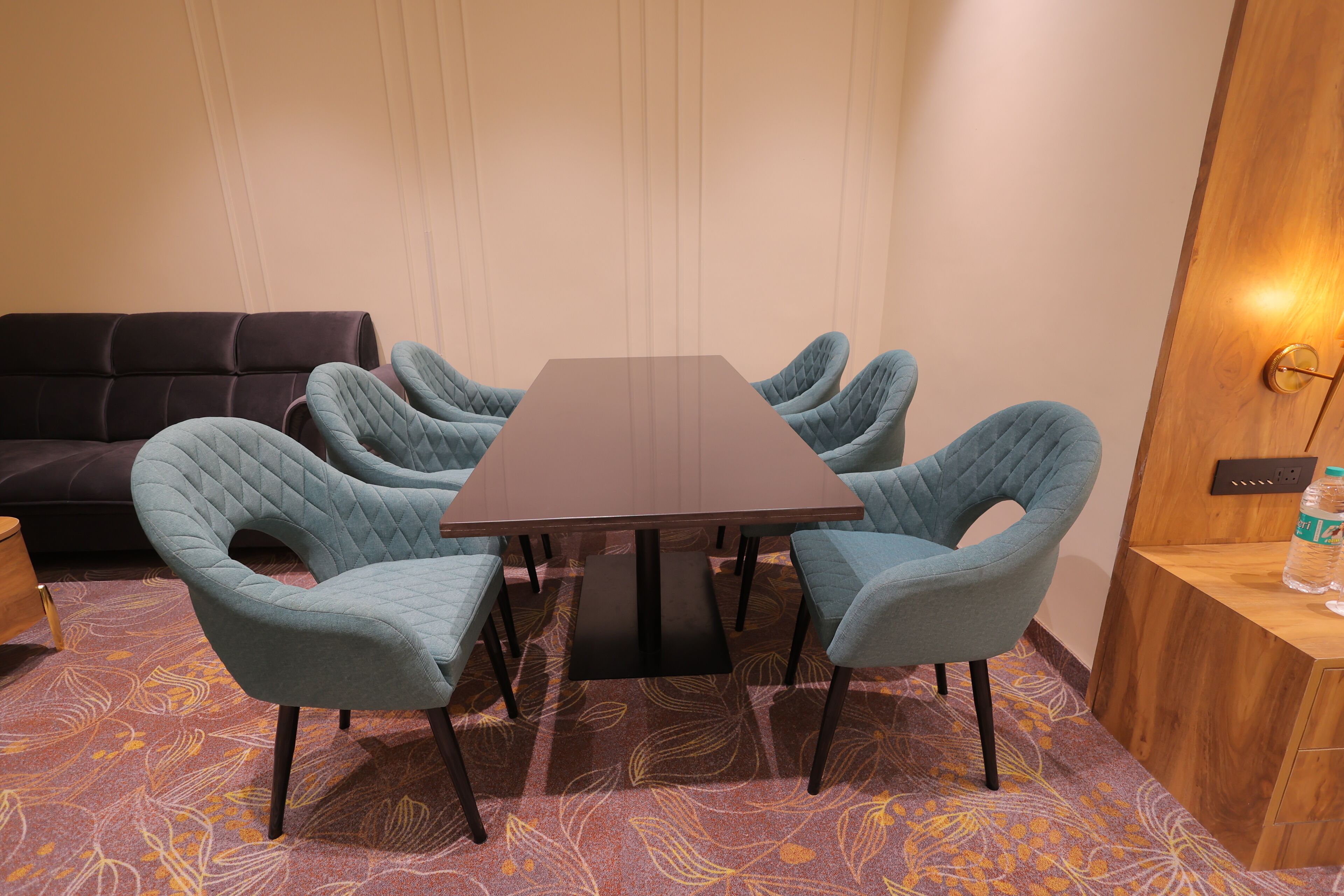 A conference room with a rectangular table, six upholstered chairs, a dark sofa, and a patterned carpet.