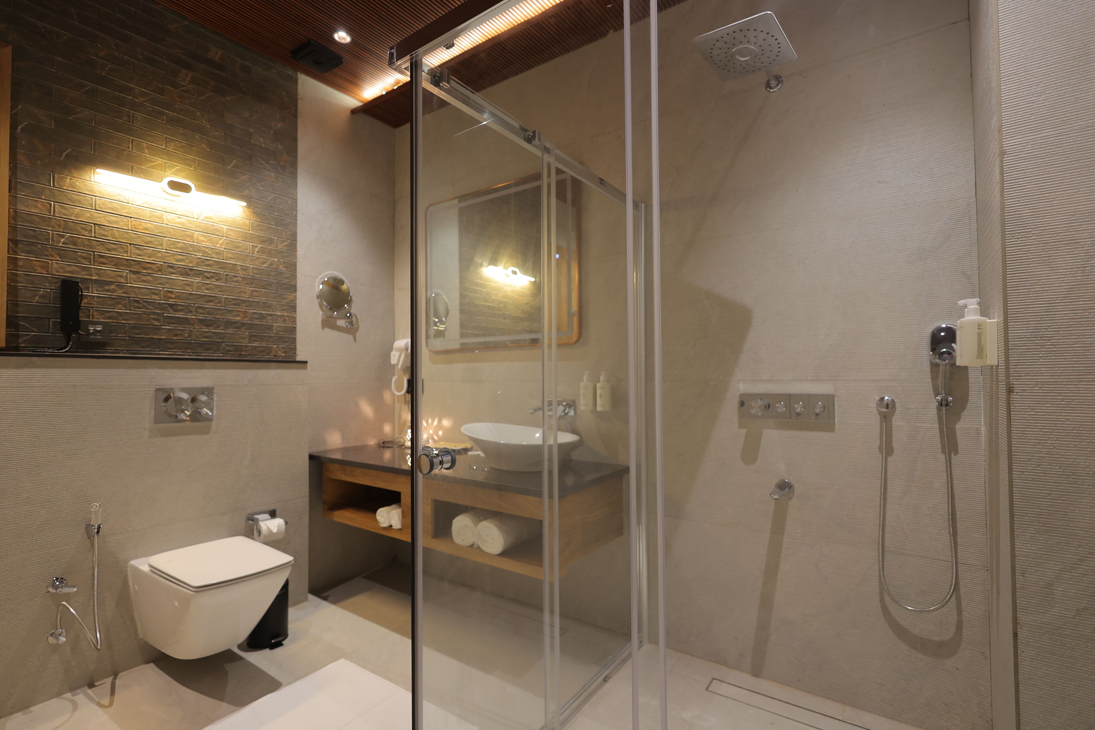 Un baño moderno con ducha de vidrio, inodoro blanco y tocador de madera con lavamanos.
