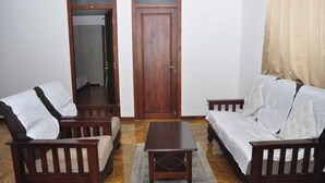 A room with two wooden sofas, a small wooden table, and a door with a number above it. - Srivari Studio Apartment (Kodaikanal)