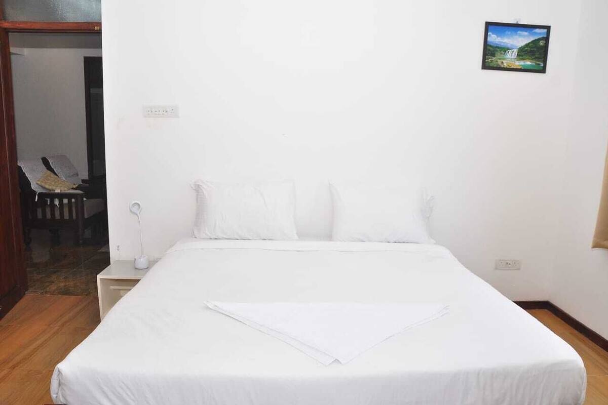 A hotel room with a large bed, a bedside table with a lamp, and a small picture on the wall.