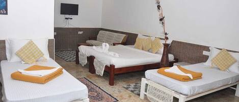 A hotel room with two single beds, a sofa bed, a TV, and a decorative plant.