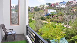 A balcony with a view of a hillside with colorful houses. - Srivari Studio Apartment (Kodaikanal)