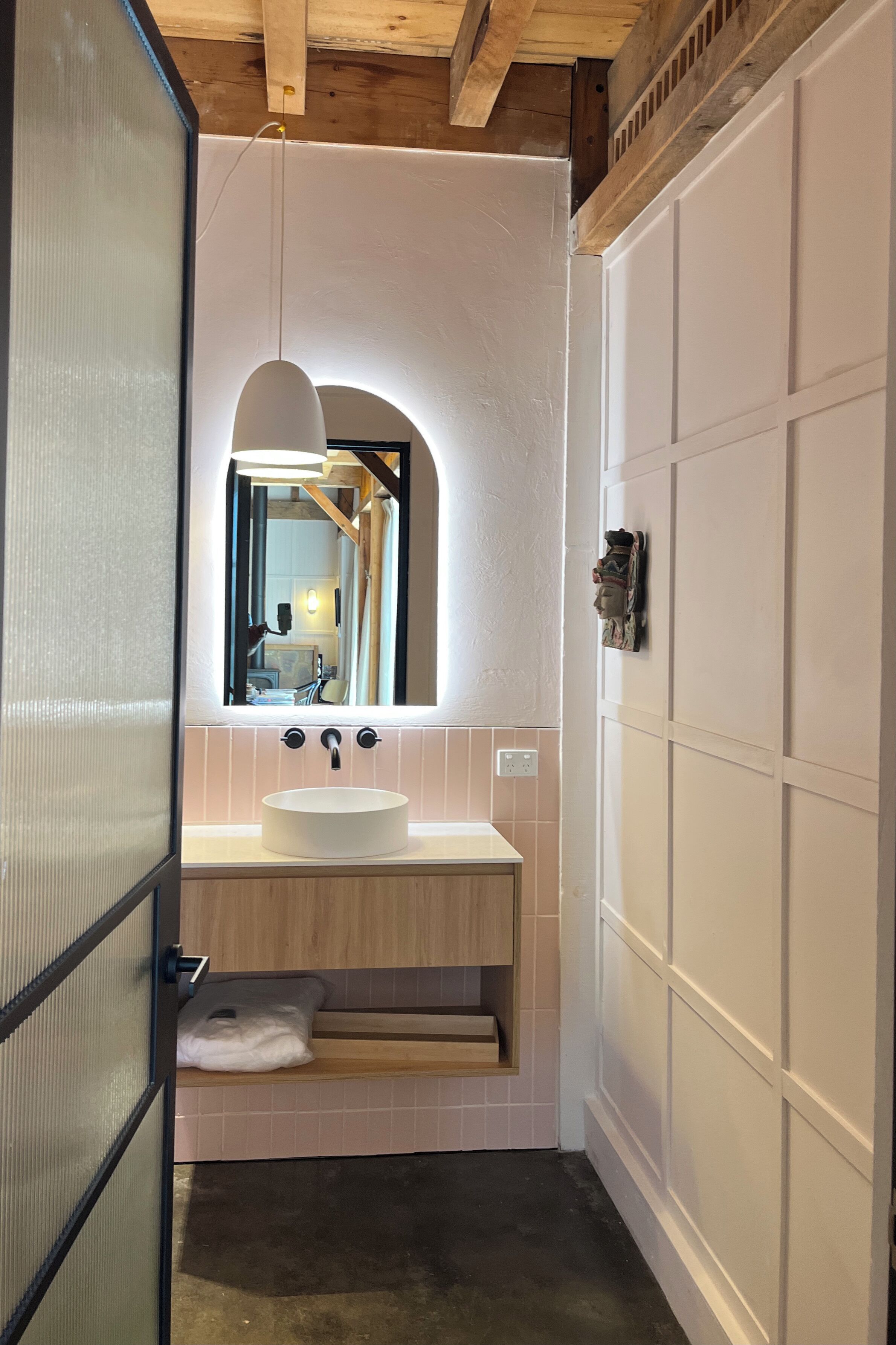 A compact bathroom with a white sink, a mirror, and a wooden ceiling.