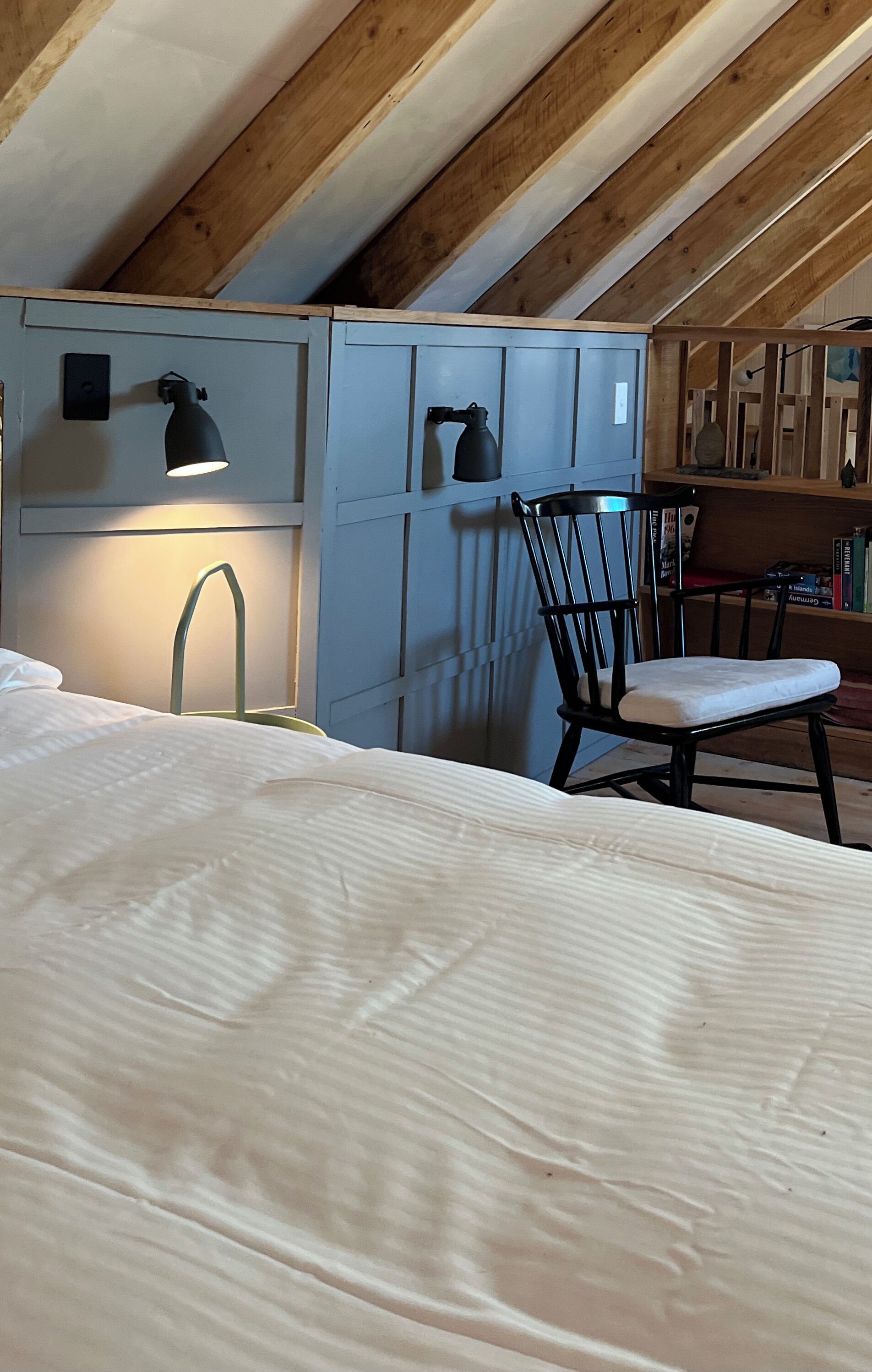 Et soveværelse med seng, stol, skrivebord med lampe og bogreol.