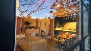 A modern interior with a sofa, dining table, and kitchen area visible through a glass window. - The Barn at Stonewalls - Farm stay in 25 acres In Daylesford (musk)