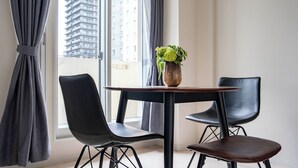 A modern room with a round table, two black chairs, a potted plant, and a view of a tall building through the window. - BELLE NEIGE 401 (Sapporo)