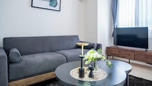 A modern living room with a grey sofa, a round coffee table with decorative items, a TV on a wooden stand, and a window with curtains. - BELLE NEIGE 401 (Sapporo)