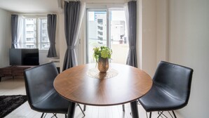 A dining area with a round table, two chairs, a vase with flowers, and a view of buildings through a window. - BELLE NEIGE 401 (Sapporo)