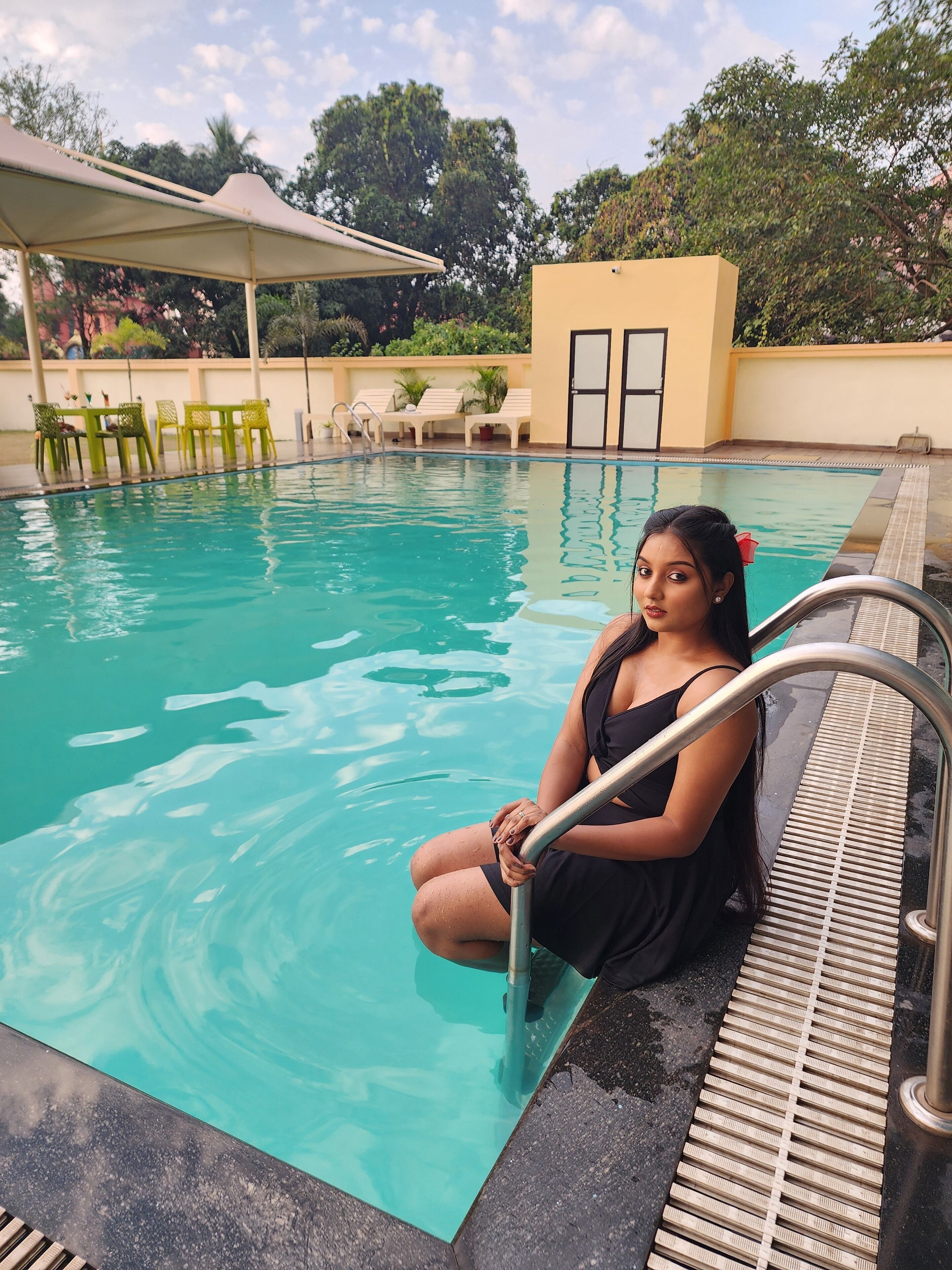 Zona de piscina con una persona sentada al borde, un área de descanso cubierta y un edificio con una puerta.