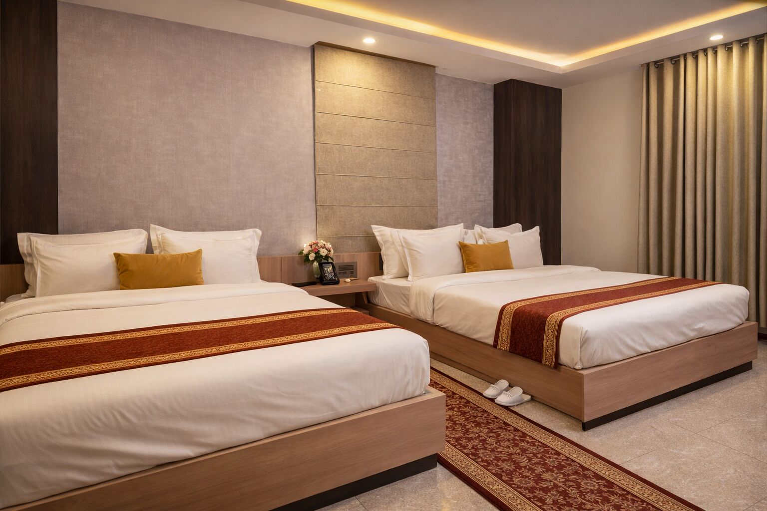 A hotel room with two beds, a wooden headboard, a nightstand with a lamp, and a decorative rug.