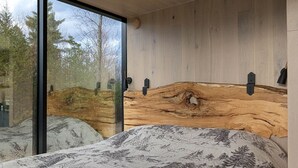 Ett modernt sovrum med en stor säng, en sänggavel i trä och utsikt över träd genom stora fönster.