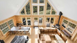 A spacious loft-style room with a large dining table, a sofa, and a fireplace. - Fox Run Log Cabin~ LUXE~Asheville~Dutch Cove (Canton)