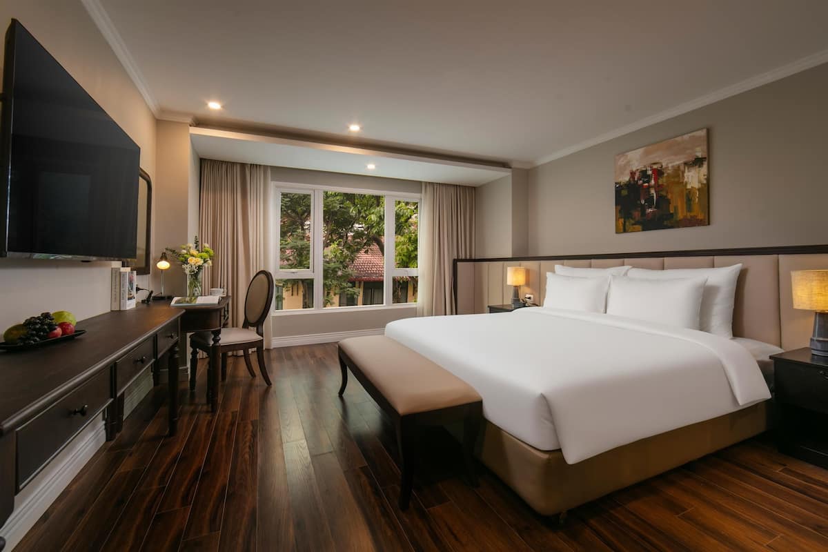 Une chambre d’hôtel avec un grand lit, un bureau avec une chaise, une télévision et une fenêtre avec des rideaux.
