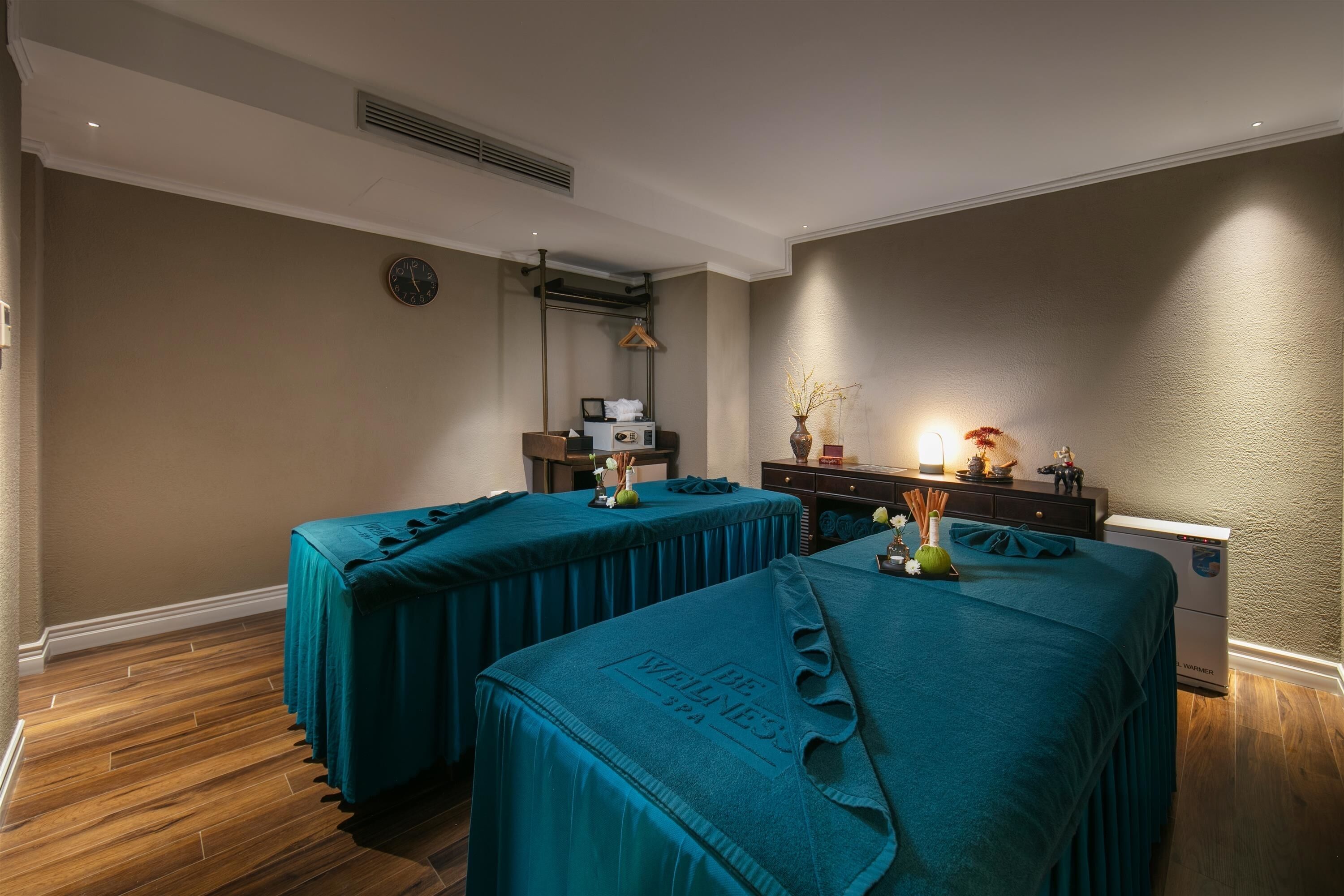 Un cuarto de spa con dos camillas de masaje, un reloj en la pared, un calentador y un mueble pequeño con objetos decorativos.