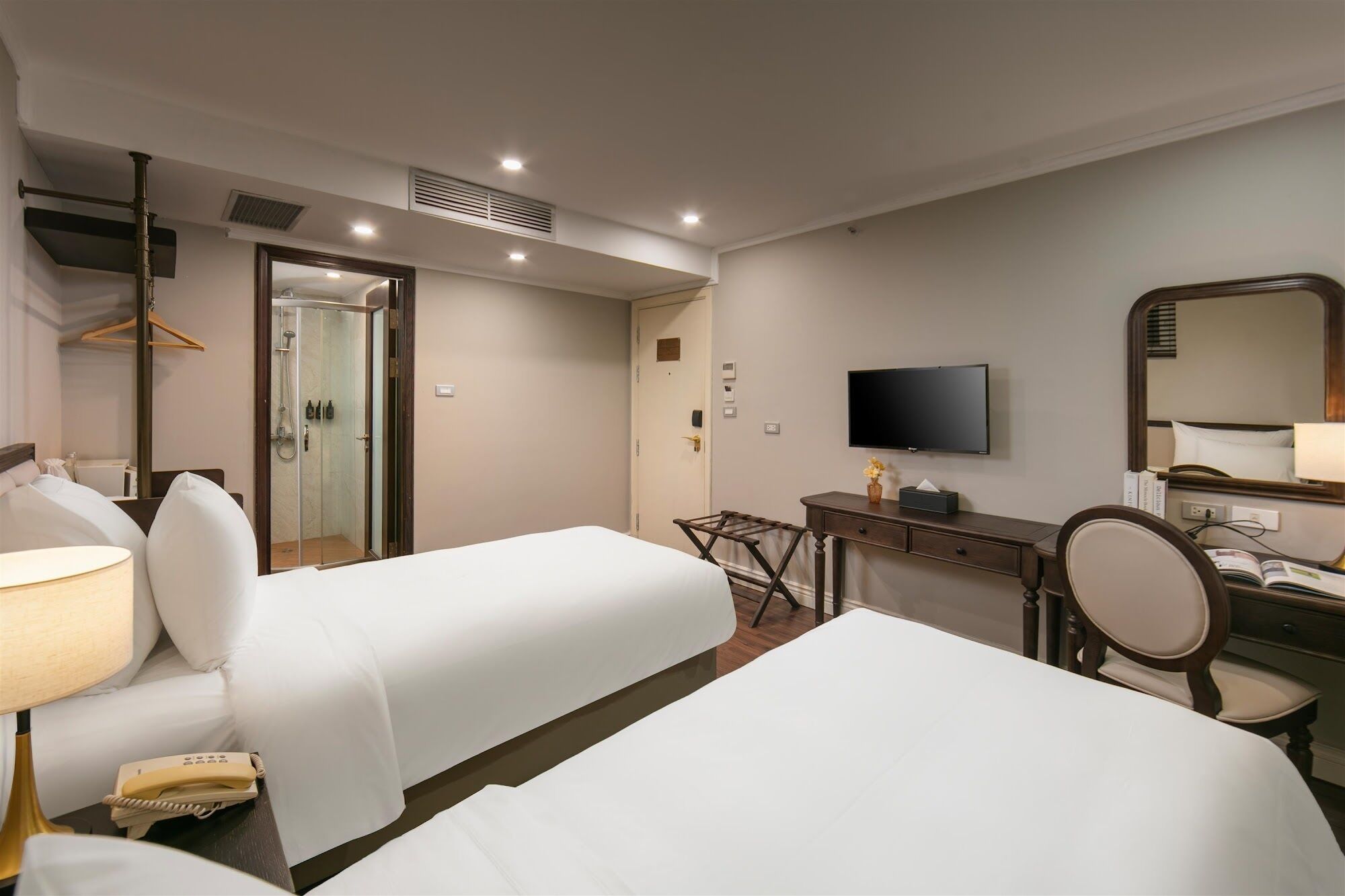 A hotel room with two beds, a desk, a chair, a television, and a mirror.