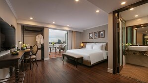 Ein Hotelzimmer mit einem großen Bett, einem Schreibtisch mit Stuhl, einem kleinen Tisch ebenfalls mit Stuhl, einem großen Spiegel und Blick auf die Stadt.