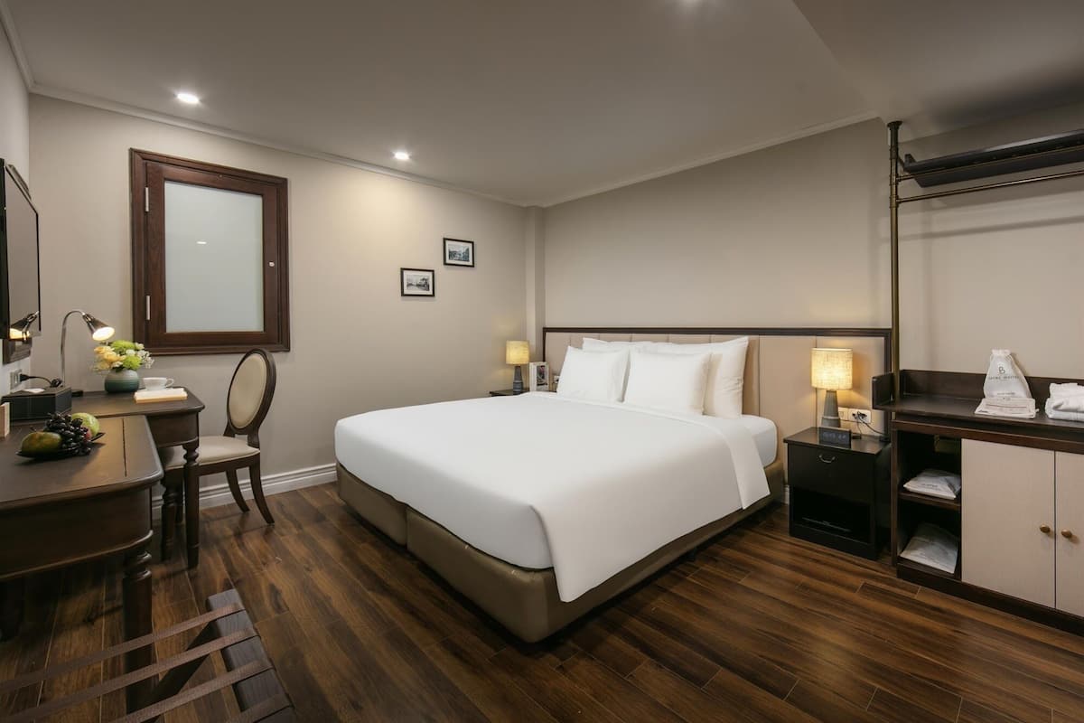 Une chambre d’hôtel avec un grand lit, un bureau avec une chaise, une table de chevet avec une lampe et une armoire.