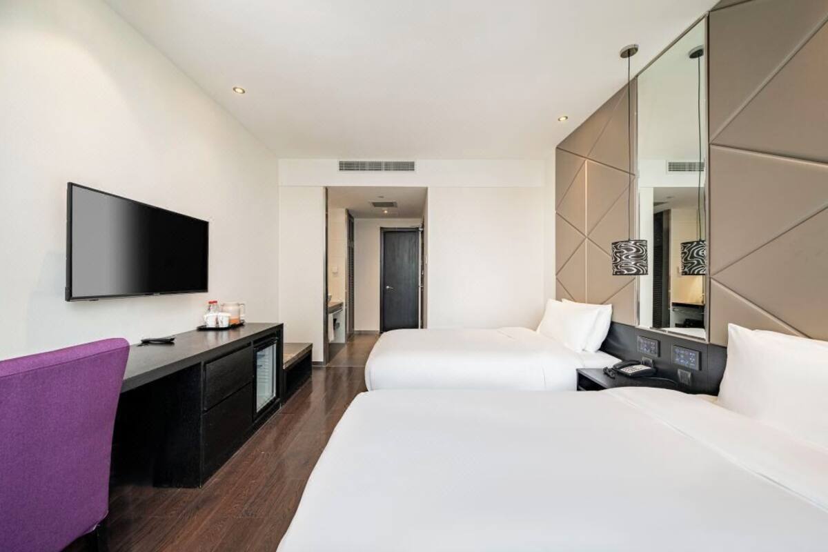 Une chambre d’hôtel avec deux lits, un téléviseur à écran plat, un bureau avec une chaise et un grand miroir.