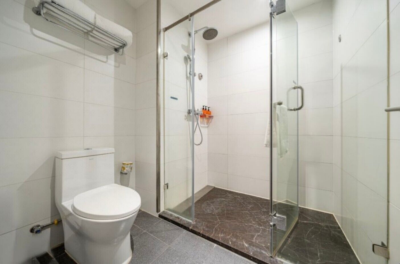 A bathroom with a toilet, a shower with a glass door, and a marble floor.