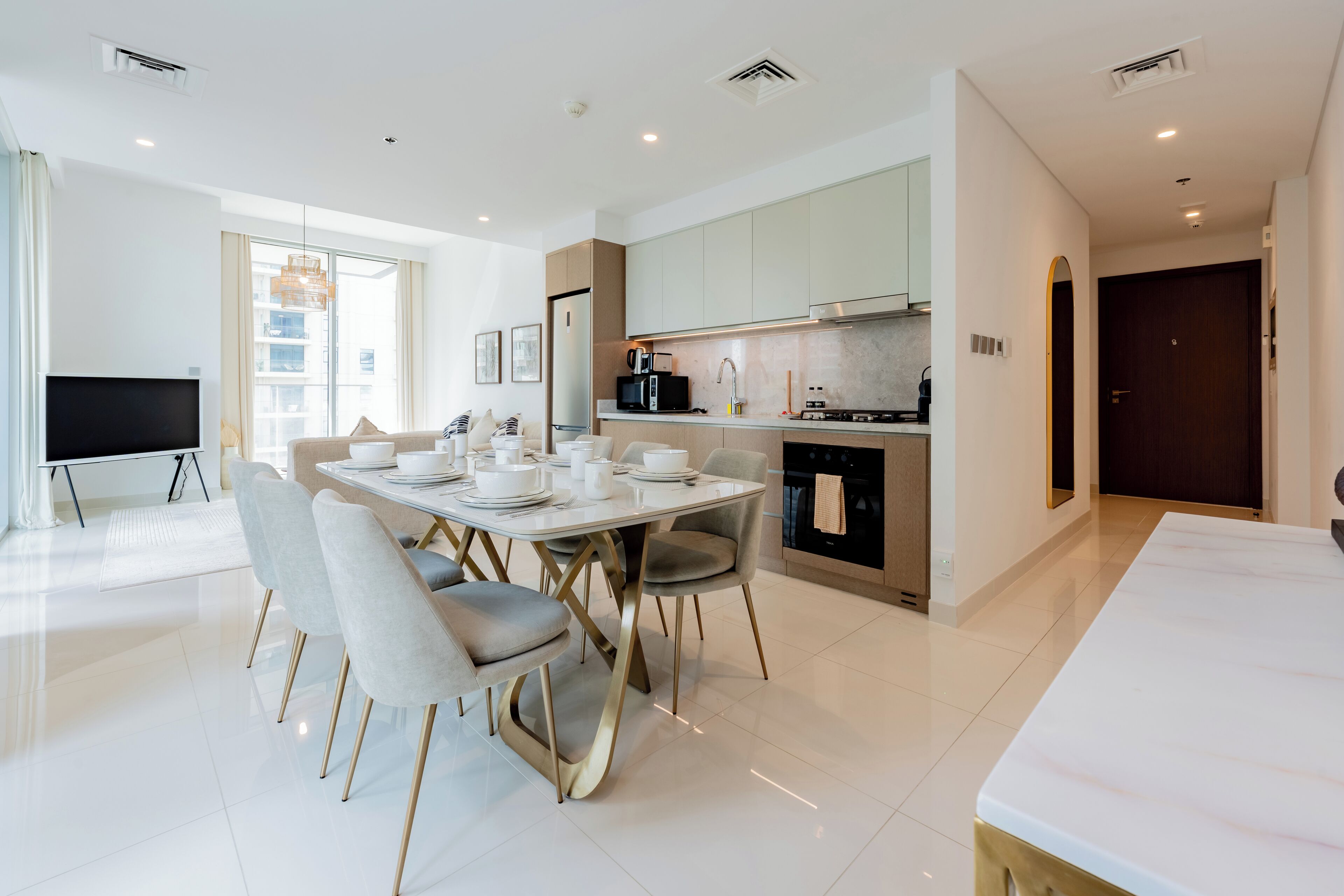 A modern kitchen with a dining area, featuring a large table with chairs, a TV, and a kitchen counter with appliances.