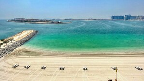 A coastal area with a sandy beach, a clear blue sea, and a distant cityscape. - Beach Isle Residences- Emaar Beachfront (Dubai)