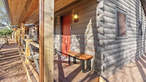 A log cabin with a wooden porch, a bench, and a red door. - Timber Lodge Cabins 31 (Colorado Springs)