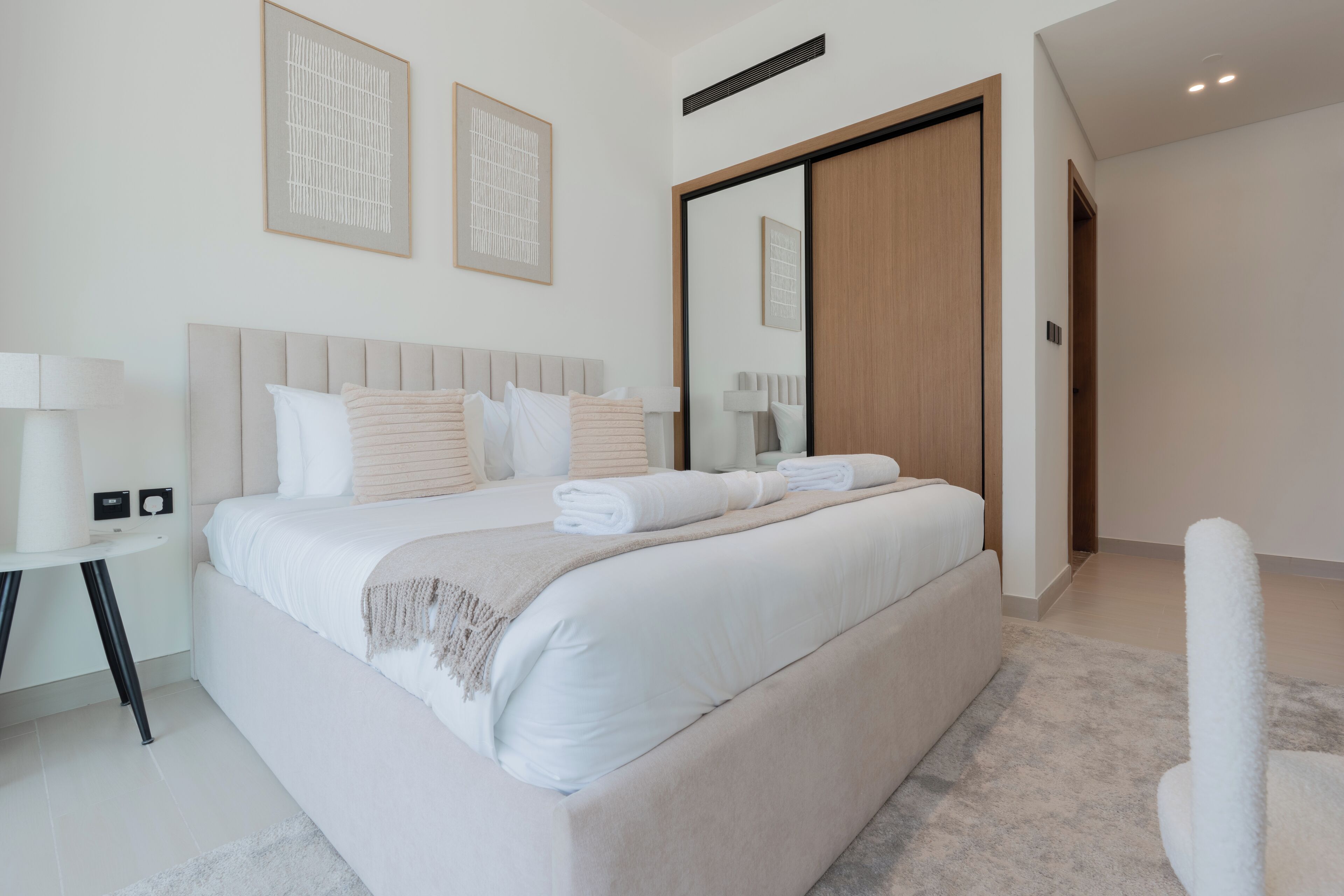 A modern bedroom with a large bed, a bedside table, a mirror, and a wardrobe.