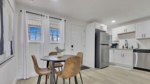 A modern kitchen with white cabinets, a stainless steel refrigerator, and a dining area with a round table and four chairs. - The Penick Getaway Su (Reynoldsburg)