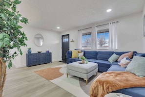 A modern living room with a blue sofa, a grey ottoman, and a blue cabinet. - The Penick Getaway Su (Reynoldsburg)