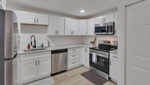 A modern kitchen with white cabinets, stainless steel appliances, and a granite countertop. - The Penick Getaway Su (Reynoldsburg)