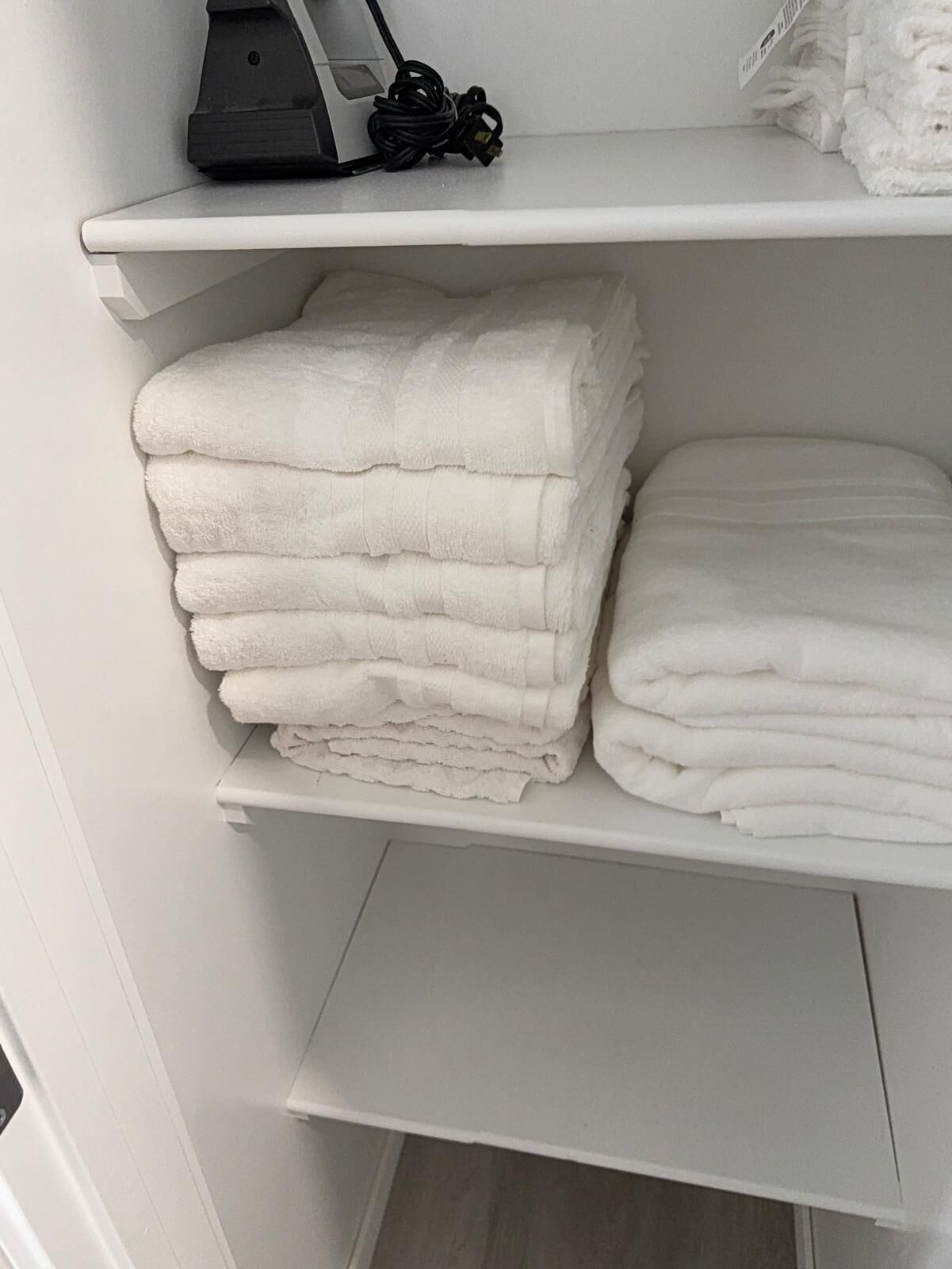 Een witte plank met opgevouwen witte handdoeken en een zwart apparaat erboven.