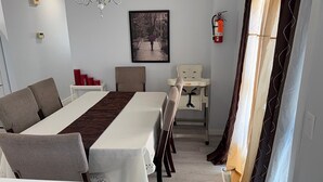 A dining area with a long table, chairs, a chandelier, a framed picture, a fire extinguisher, and a baby changing station. - Beautiful Renovated Bi-level  Home close to shopping, transit, & Rec Centre (Calgary)