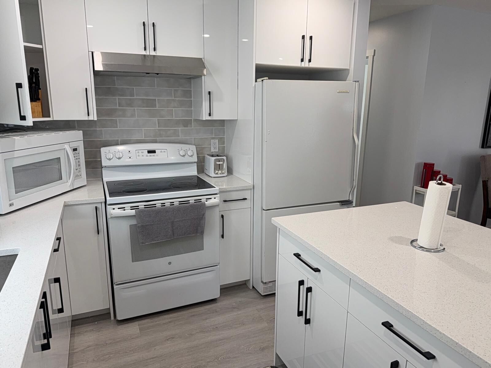 A modern kitchen with white cabinetry, a built-in oven, a microwave, and a refrigerator.