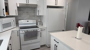 A modern kitchen with white cabinets, a built-in oven, a microwave, and a refrigerator. - Beautiful Renovated Bi-level  Home close to shopping, transit, & Rec Centre (Calgary)
