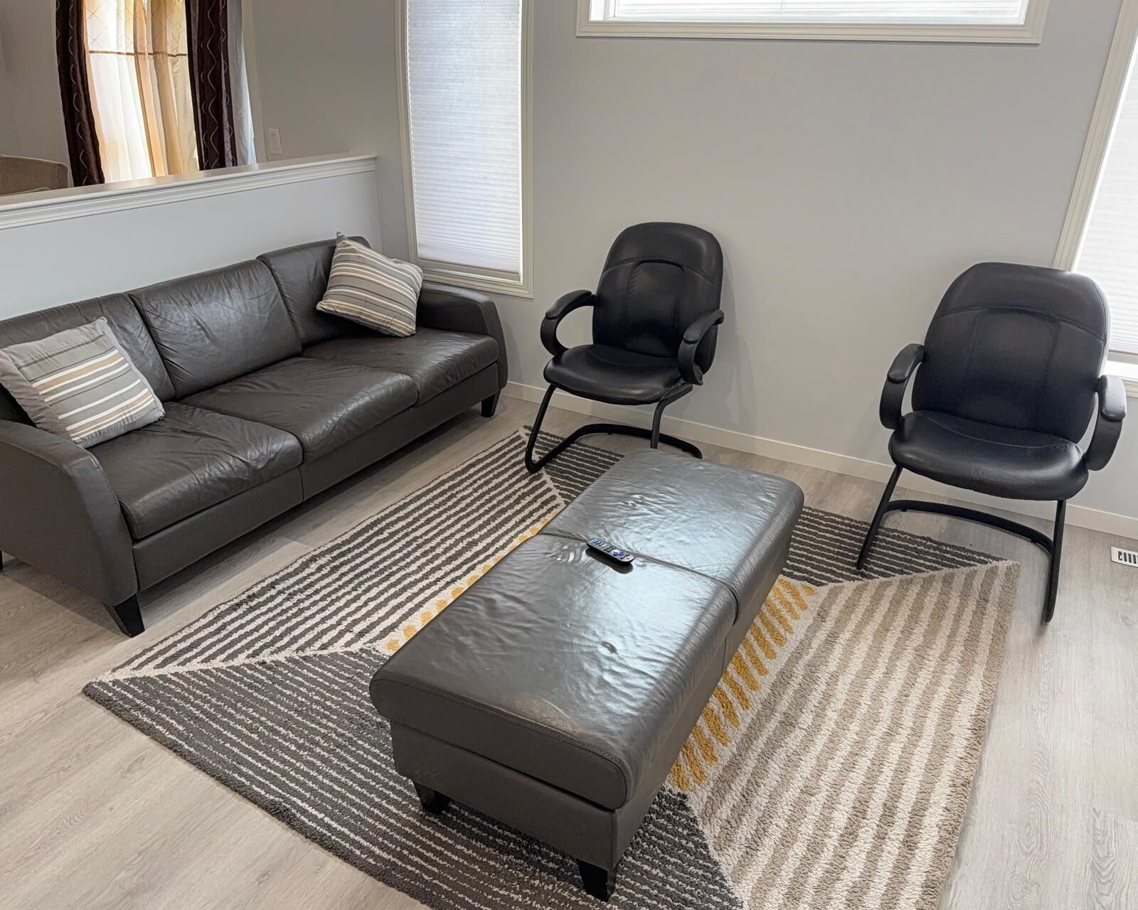 Un salon moderne avec un canapé en cuir, deux chaises de bureau noires et un pouf assorti.