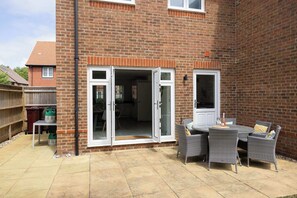 A brick house with a patio area featuring a table and chairs, a sliding glass door, and a small outdoor kitchen setup.