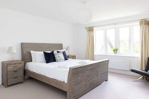 A bedroom with a wooden bed, bedside tables, a lamp, and a window with curtains. - Modern Family Retreat Nr Beaches and Marina (Birdham)